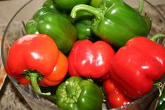 red and green peppers in a glass bowl on a counter top next to other vegetables