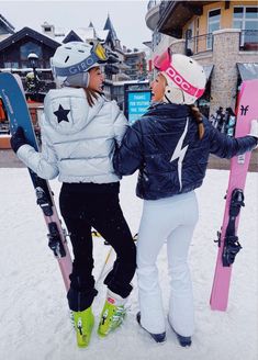 two women standing in the snow with their skis