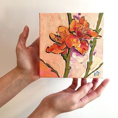 a person holding up a small painting with flowers on it