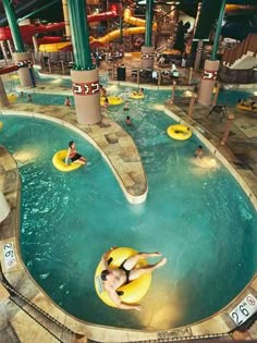 people are swimming in an indoor pool with yellow rafts and water slides on the sides