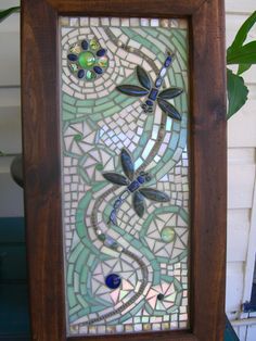 a stained glass panel with dragonflys on it in a wooden frame next to a potted plant