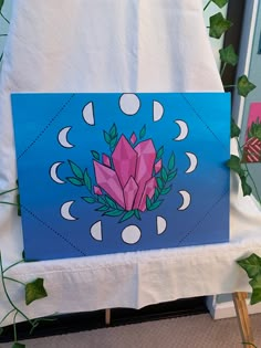 a blue and pink painting on a white table cloth next to some green plant life