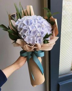 a person holding a bouquet of flowers in front of a door with blue ribbon around it