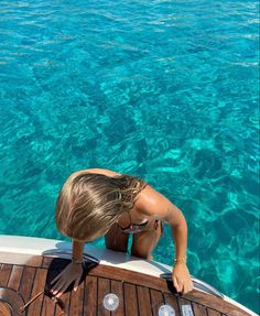 a woman standing on the back of a boat looking out at clear blue ocean water