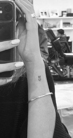 a woman with a small butterfly tattoo on her left wrist holding a cell phone up to her face