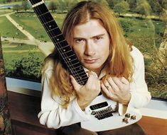 a man with long hair is holding an electric guitar in front of a large window