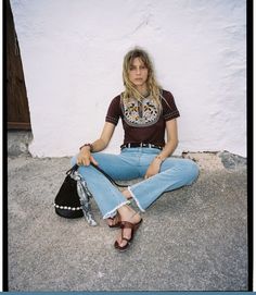 a woman is sitting on the ground with her hand in her pockets and wearing jeans