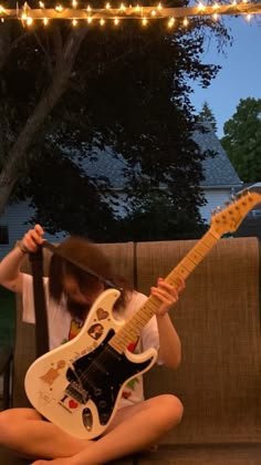 a person sitting on a couch with a guitar in their lap and lights strung above them