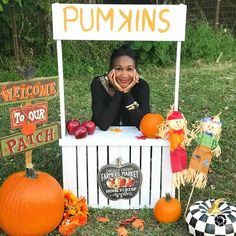 a woman sitting at a pumpkin stand in the grass with her hands on her face