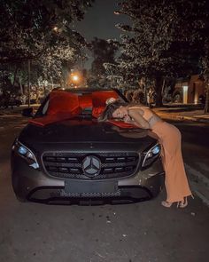 a woman leaning on the hood of a black car at night with her head down