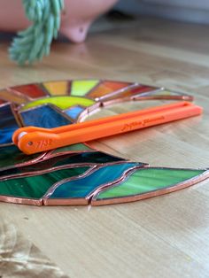 a colorful stained glass piece laying on top of a wooden table next to a pair of scissors