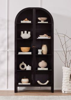 a black bookcase filled with vases and other items on top of a wooden floor