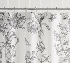 a white shower curtain with black and white floral designs on it, hanging from a metal rod