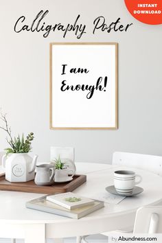 a white table topped with books and cups next to a framed poster that says, i am enough