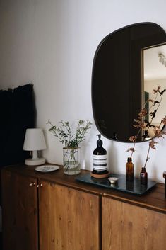 a mirror on top of a wooden dresser next to a vase with flowers in it