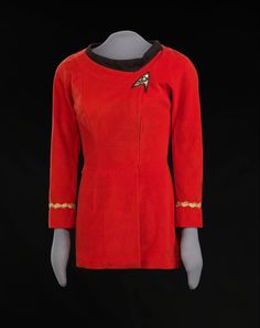 a red dress with gold trims and a star trek insignia on the chest, in front of a black background