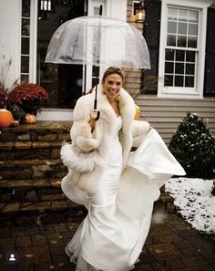 a woman in a white dress and fur coat holding an umbrella