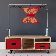 a wooden cart with two red drawers and a butterfly on it's wings, in front of a gray wall