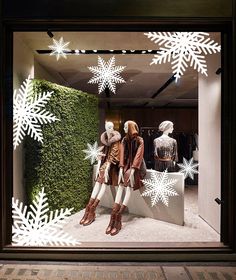 two mannequins dressed in winter clothes and snowflakes are seen through a window