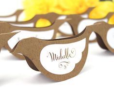 some paper bird shaped place cards with name tags on them and yellow flowers in the background