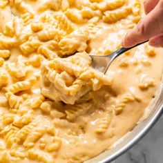 a person spooning macaroni and cheese into a pan