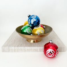 a bowl filled with ornaments sitting on top of a white table next to a red and green ornament