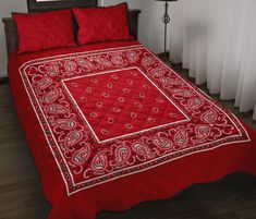 a red bedspread with a white border and paisley print on the edges, in front of a window