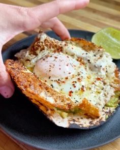 a person is reaching for an egg in a toasted sandwich on a black plate