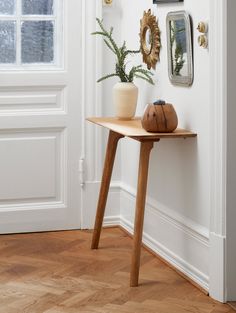 a wooden table sitting in front of a white wall next to a potted plant