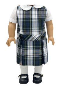 the doll is wearing a plaid dress and black shoes, while she has her hands in her pockets