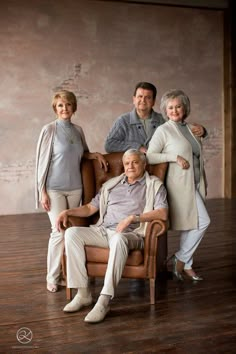 an older man sitting in a chair with two women and one man standing next to him