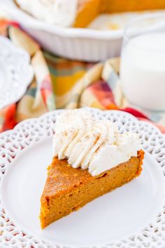 a slice of pumpkin pie on a white plate with whipped cream around it and a glass of milk in the background