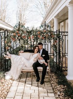 a bride and groom sitting on a bench in front of an iron gate with roses