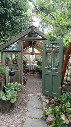 a small garden shed with an open door and green plants in the front, surrounded by greenery