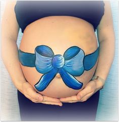 a pregnant belly with a blue bow painted on it's side and hands around it