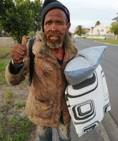 a man is standing on the side of the road holding a bag and giving thumbs up