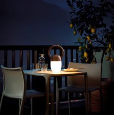 two chairs and a table on a balcony at night with lemons in the background