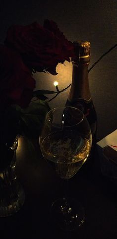 a bottle of wine sitting next to a glass filled with water and roses on a table