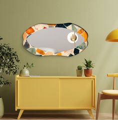 a mirror that is on the side of a wall next to a yellow cabinet and potted plant