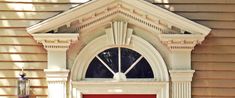 a red door is in front of a tan building with a clock on it's side