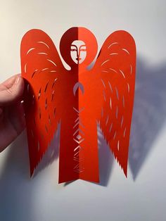 someone is holding up a red paper cut out of an angel's head and wings