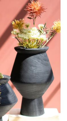 two black vases with flowers in them on a table