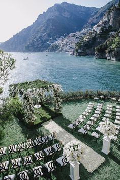 an outdoor ceremony setup with white flowers and black chairs on the grass by the water