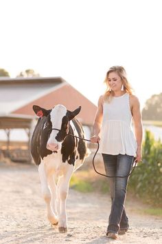 a woman leading a cow down a dirt road