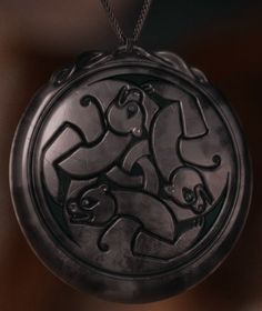 a black pendant with an intricate design hanging from a chain on a dark background,