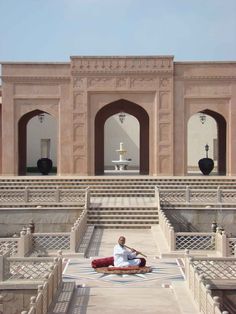 a man sitting on top of a rug in front of a building with arches and stairs