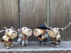 three little sheep figurines with hats and bells on their heads are lined up against a wooden fence