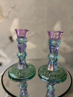 two glass candlesticks sitting on top of a round table next to each other