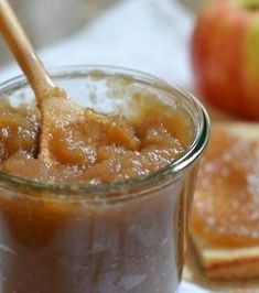 an apple jam is in a glass jar with a wooden spoon sticking out of it