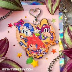 a key chain with cartoon characters on it sitting next to some flowers and stars in the background